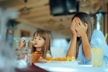 Çocuk restoranda pizza yiyor ve anne yüzünü kapatıyor.