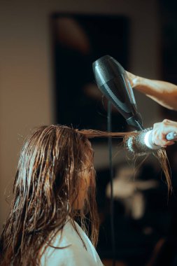 Kuaför, saç fırçası ve saç kurutma makinesi kullanarak ıslak saç kurutur.