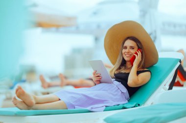 Deniz kenarında güneşlenen bir kadın Tablet ve telefon üzerinde çalışıyor