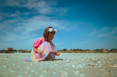 Deniz kenarında deniz kabuklarıyla oynayan küçük kız.