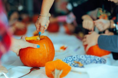 Cadılar Bayramı partisinde insanlar balkabağı oyuyor.