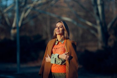 Paltolu ve örgülü yelekli kadın Sonbahar güneşinin tadını çıkarıyor