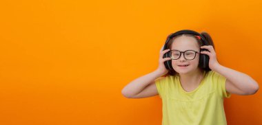 Girl with Down syndrome listens to music. Orange background. Banner