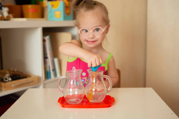 A girl with Down\'s syndrome learns to pour water from pitcher to pitcher. Early development
