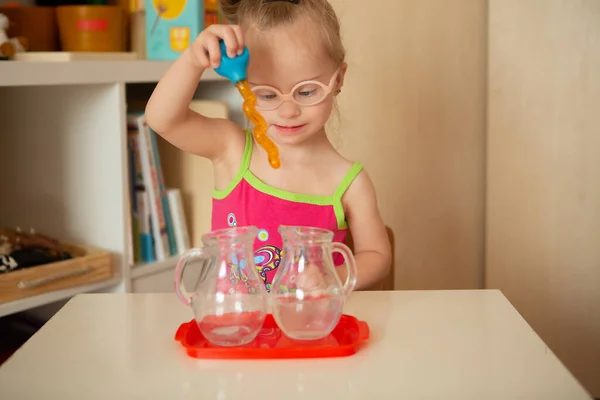 A girl with Down\'s syndrome learns to pour water from pitcher to pitcher. Early development