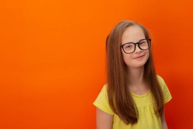 Happy girl with Down syndrome. Having fun, laughing. Funny pigtails. Studio. Portrait on a orange background