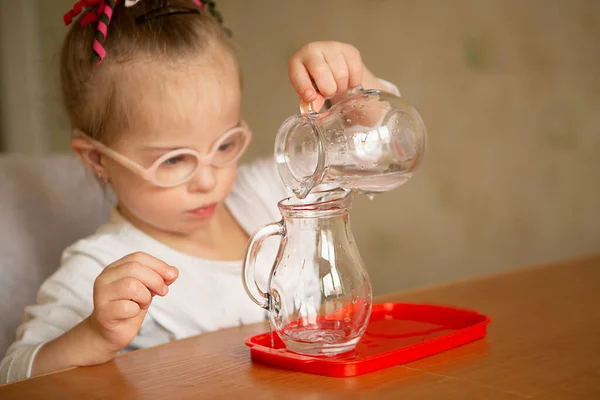 A girl with Downs syndrome learns to pour water from pitcher to pitcher. Early development