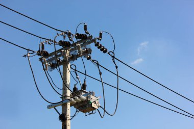 Yüksek voltajlı kablolar, yüksek voltajlı transformatöre bağlandı. Direğe monte edildi. Mavi gökyüzüne karşı.