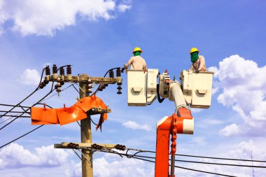 Hava platformunun beşiği üzerinde çalışan elektrik mühendisliği ekibi ya da mavi gökyüzüne karşı yüksek voltaj iletim hatlarını tamir eden vinç.