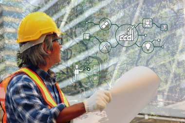 Güvenlik formundaki işçi planlarını ve şantiyeye bakıyor.