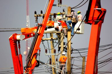 Hava platformunun beşiği ya da vinç üzerinde çalışan elektrik mühendisliği ekibi, yüksek voltajlı transformatöre bağlı yüksek voltajlı iletim hatlarını mavi gökyüzüne karşı direğe monte etti.