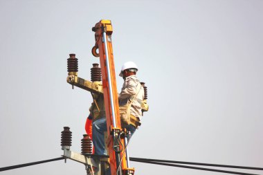 Elektrik işçisi direğe yüksek voltaj hattı kuruyor. İşçiler emniyet kemeri kaskı taktılar. Elektrik direğine tırmandılar ve dikkatli çalıştılar.