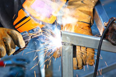 İnşaat alanındaki kaynakçı çelik yapısını kapatın. Kaynakçı deri eldiven ve kask giyerken işçi kaynakçıları elektriği ve sıcaklığı korur.