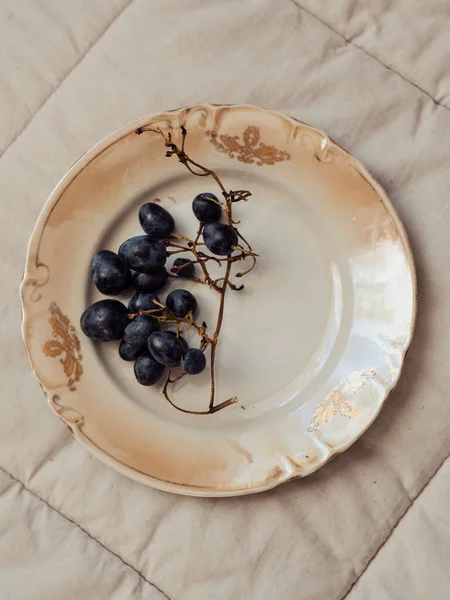 Minimal still life: Vertical straight from above close up shot of black grapes on a vintage beige plate.