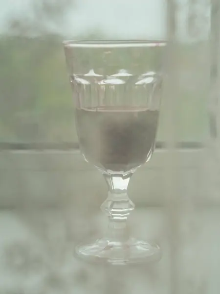 stock image Vertical close up view of a glass of red wine on a windowsill behind a white laced curtain.