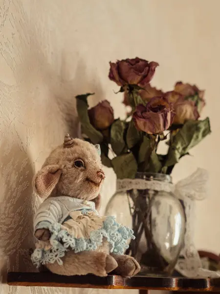 Klasik Zarafet: Teddy Lamb ve Güller: Mavi dantelli bir elbise giymiş sevimli bir Teddy Lamb 'in yer aldığı dikey ve durgun bir hayat, her ikisi de kırsal ahşap bir rafta dinlenen bir buket kurutulmuş gülle birlikte.