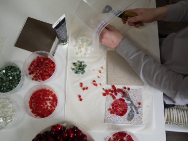 Crafting Mosaic: Man using pliers to shape a red mosaic piece to the desired form. Horizontal straight from above close up. clipart