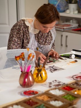 Mosaic Workshop: Vertical table top shot captures an elegant woman crafting a floral mosaic pattern amidst a messy colourful creative chaos on the table. clipart