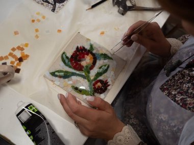 Mosaic Workshop: A horizontal straight from above close-up shot captures a woman's hands crafting a floral mosaic pattern. clipart