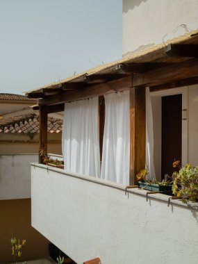 Vertical view of a cozy balcony corridor with white curtains and doors in an Italian multi story building in Olbia, Sardinia, Italy. clipart