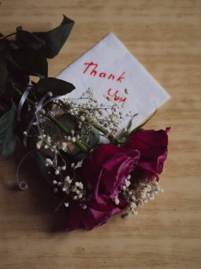 A Bouquet of Roses and a Handwritten 'Thank You' on a Paper Napkin against the Wooden Table Backdrop clipart