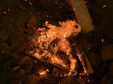 Ateş karanlıkta, yakın planda yanıyor. Ateşin kırmızı dilleri bahçede yanıyor. Kavram: ısı, karanlıkta ışık, ısı