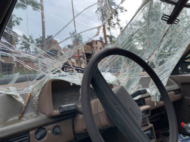 Kırık araba ön camı. Araba savaşta hasar görmüştü. Evin arka planında patlayan nakliye aracı..