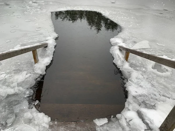 A hole in the ice for swimming on the lake. Steps with railings leading to the ice hole. Concept: winter swimming in the hole.