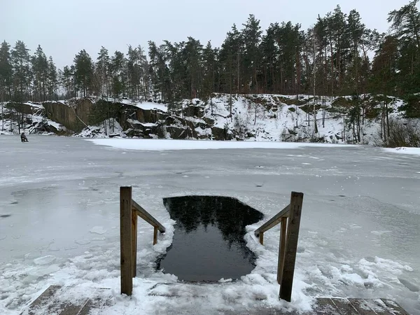 A hole in the ice for swimming on the lake. Steps with railings leading to the ice hole. Concept: winter swimming in the hole.
