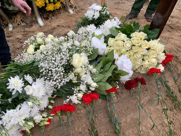 The grave in the cemetery is lined with flowers. Lots of white and red flowers on the grave. Concept: funeral of a loved one