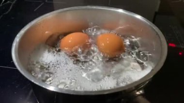 Kaynar suda tavuk yumurtası, yakın plan. Tencerede tavuk yumurtasıyla kaynar su. İndüksiyon sobasında yemek pişirmek..