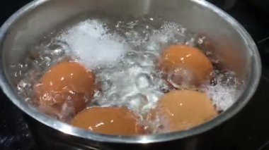 Kaynar suda tavuk yumurtası, yakın plan. Tencerede tavuk yumurtasıyla kaynar su. İndüksiyon sobasında yemek pişirmek..