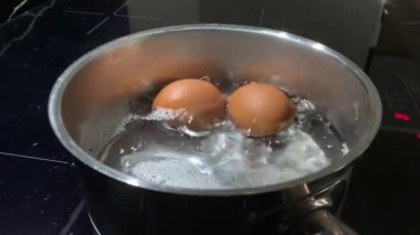 Kaynar suda tavuk yumurtası, yakın plan. Tencerede tavuk yumurtasıyla kaynar su. İndüksiyon sobasında yemek pişirmek..