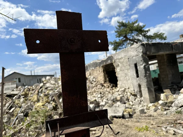The ruins of a residential building after shelling. Cross on the background of a burnt house. Concept: Cross of Christ, suffering from war.