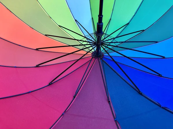 The open umbrella is bright, multi-colored, close-up. Large umbrella from the rain in all colors of the rainbow. Background texture: colored umbrella mechanism.