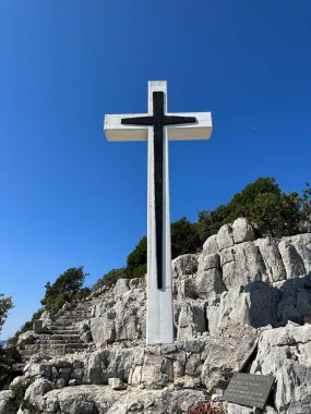 Denizin arka planında büyük bir haç var. İsa 'nın Haçı dağda yükseliyor. Hırvatistan, Ugljan adası, kalenin yıkıntıları yakınında, 7 Eylül 2023.