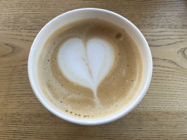 Kalp şeklinde köpüklü bir fincan cappuccino. Kağıt bardak sütlü kahve ya da Americano kahvesi. Lokantada masada güzel bir kahve servisi..