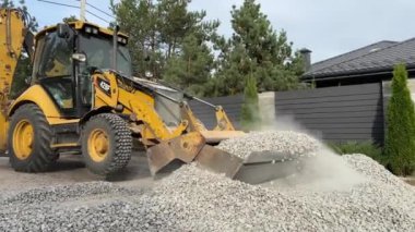 Bir kazıcı bir kovayla ezilmiş taşı topluyor. Traktör toprak bir yolu dümdüz eder. Yol çalışması, orman yolunun yakınındaki makineler. Ukrayna, Kiev bölgesi, Irpen şehri, 12 Ekim 2023