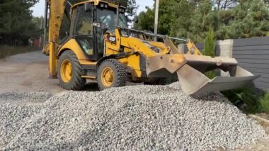 Bir kazıcı bir kovayla ezilmiş taşı topluyor. Traktör toprak bir yolu dümdüz eder. Yol çalışması, orman yolunun yakınındaki makineler. Ukrayna, Kiev bölgesi, Irpen şehri, 12 Ekim 2023