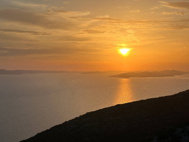 Gün batımı denizin ve dağların ardında. Deniz suyunda batan güneşin yansıması, dağdan görüş..