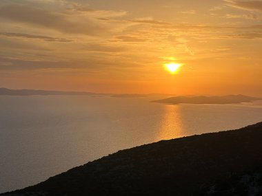 Gün batımı denizin ve dağların ardında. Deniz suyunda batan güneşin yansıması, dağdan görüş..