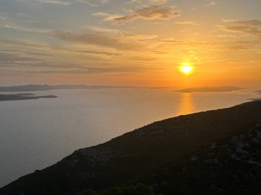 Gün batımı denizin ve dağların ardında. Deniz suyunda batan güneşin yansıması, dağdan görüş..