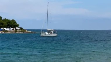 Mavi denizde beyaz bir yelkenli yelken açar. Adriyatik denizinin huş ağacı suyunda yelkenli. 27 Haziran 2024 'te Hırvatistan kıyısı açıklarındaki Preko adasında tatil gezisi