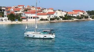 Mavi denizde beyaz bir yelkenli yelken açar. Adriyatik denizinin huş ağacı suyunda yelkenli. 27 Haziran 2024 'te Hırvatistan kıyısı açıklarındaki Preko adasında tatil gezisi