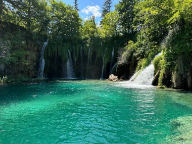 Hırvatistan 'ın Plitvice Gölleri' nde büyüleyici bir şelale, yazın bereketli dağ manzaralarında güzel bir şekilde yuvarlanarak, doğanın sükunetini ve korkusunu arayanlar için çarpıcı bir zemin oluşturuyor..