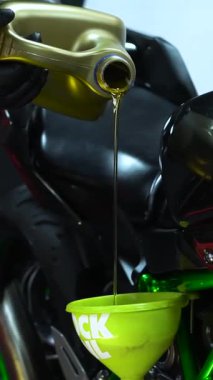 Bir kişi, motorlu aracın yeşil bacasına sıvı ekliyor, muhtemelen motor için yağı dolduruyor ya da jant ya da lastik gibi diğer parçaları.