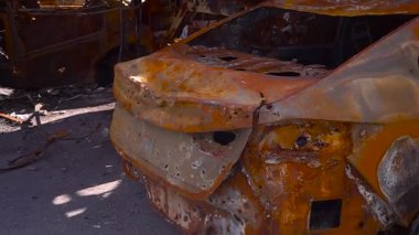 Paslı bir otomobili olan yıpranmış bir araç asfalt ve ahşap yapı malzemeleriyle çevrili yol kenarına park edilmiştir.