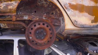 Paslı araba iskeleti olan bir aracın tepesine tünemiş yalnız bir otomotiv lastiği vardır. Alaşımlı tekerlek, aşağıdaki yıpranmış direksiyonla çelişiyor.