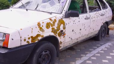 Şehir kaldırımında kurşun delikleri olan yıpranmış bir araba mermisi tehlikeli bir çevrede terk edilmiş bir aracı yansıtır.