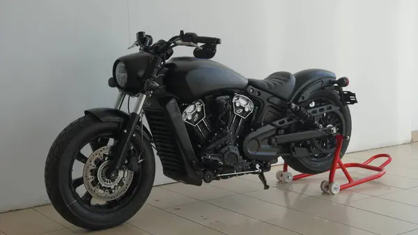 Modern, mat siyah motosiklet bir stantta sergileniyor, çarpıcı derecede gösterişli ve çekici tasarımı vurgulanıyor.